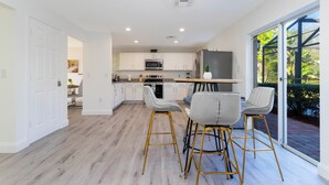 A modern kitchen with white cabinets, a stainless steel refrigerator, and a dining area with bar stools. - Beautiful 5Bd Single Family w Game Room 106 Lake Wilson Preserve (Davenport)