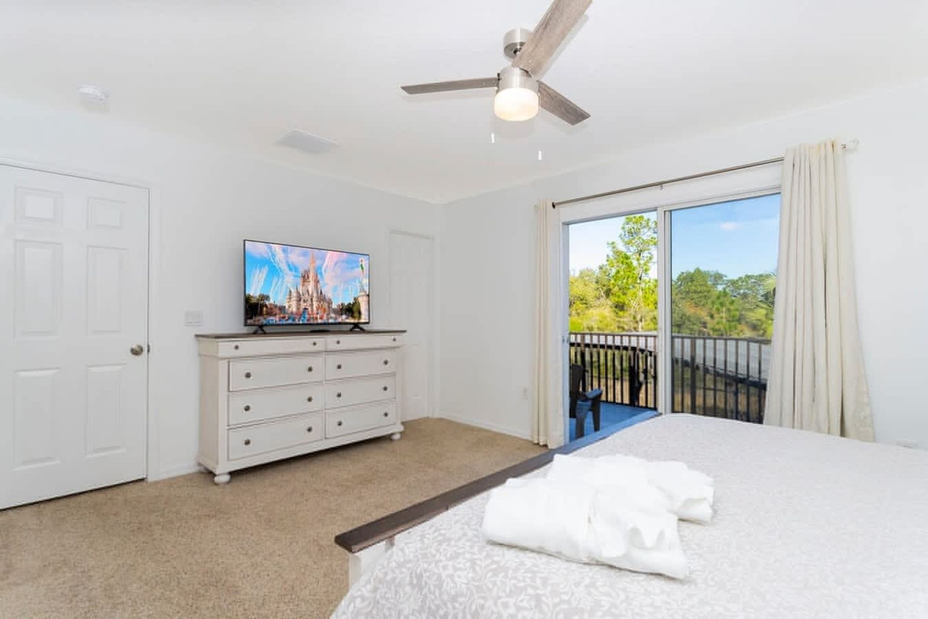 A bedroom with a bed, a dresser, a television, and a balcony with a view.