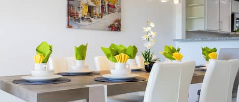 Un comedor moderno con una mesa de madera preparada para seis personas, sillas blancas y un cuadro en la pared.