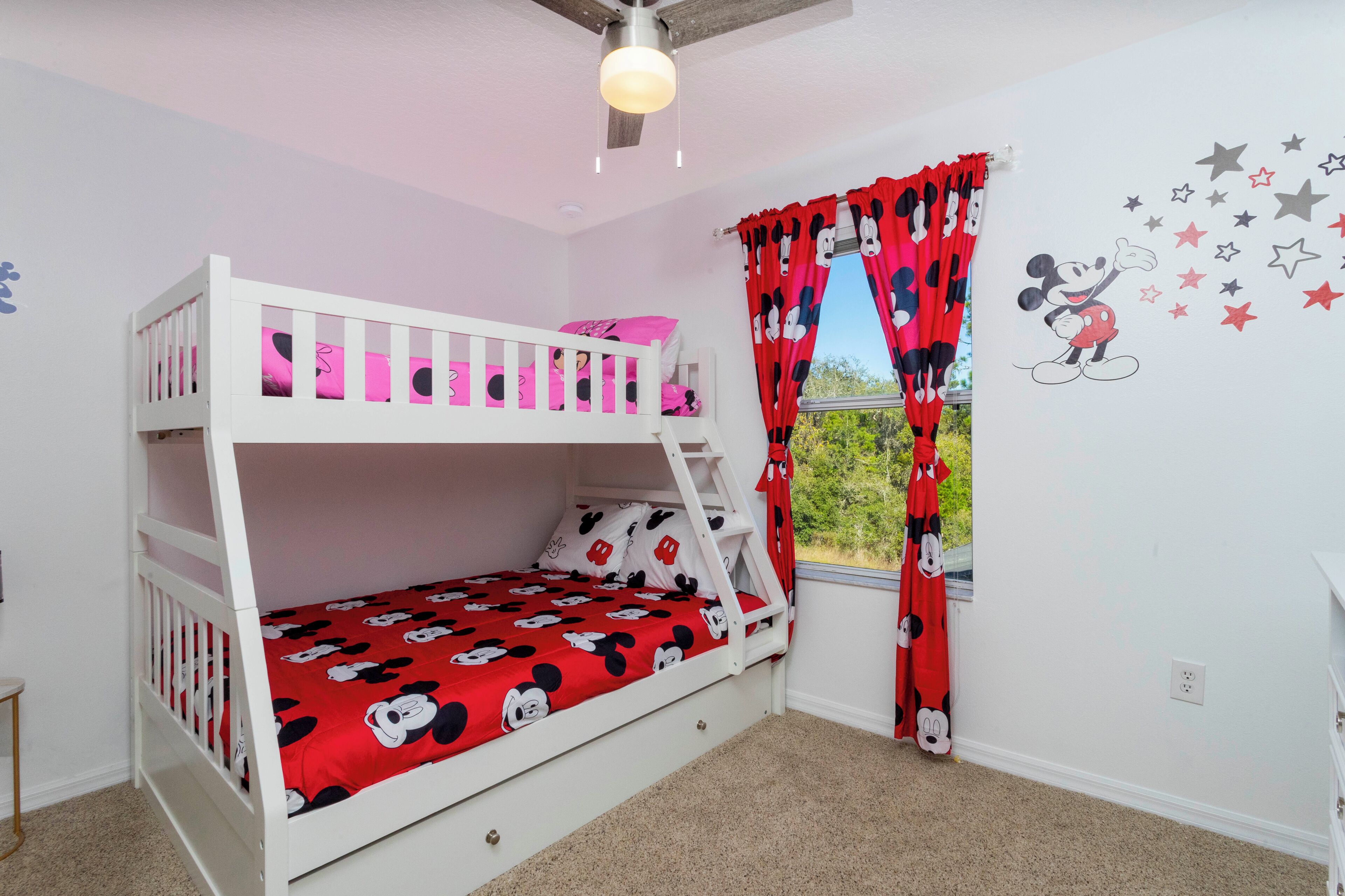 A bunk bed room with Mickey Mouse themed bedding, a window with red curtains, and a wall decal of Mickey Mouse.