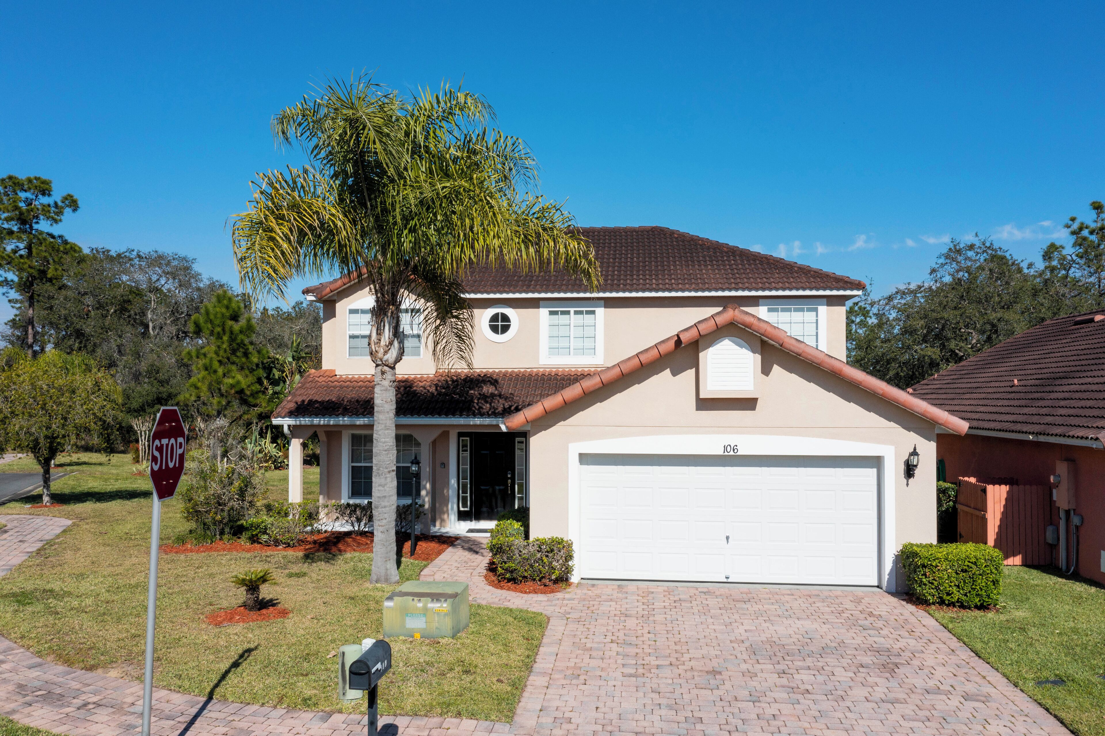 A two-story house with a white garage door, a red roof, and a stop sign in the driveway.