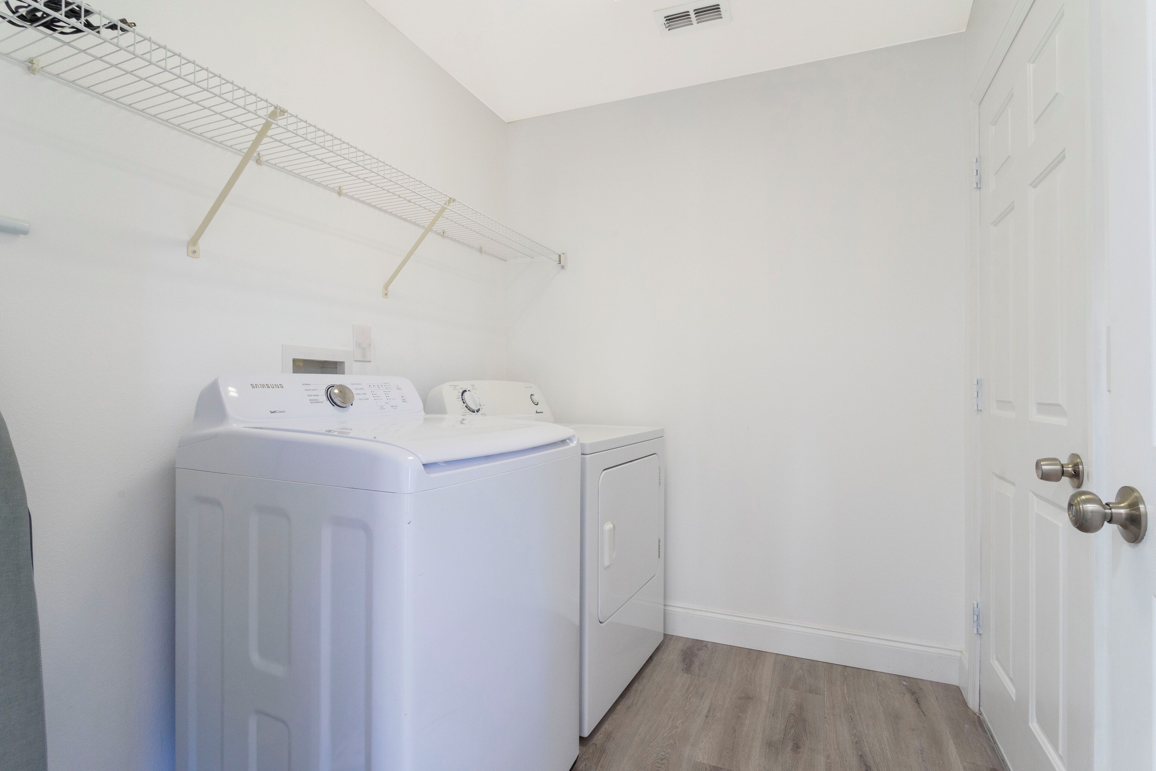 A laundry room with a front-loading washer and dryer, a drying rack, and a door with a silver handle.
