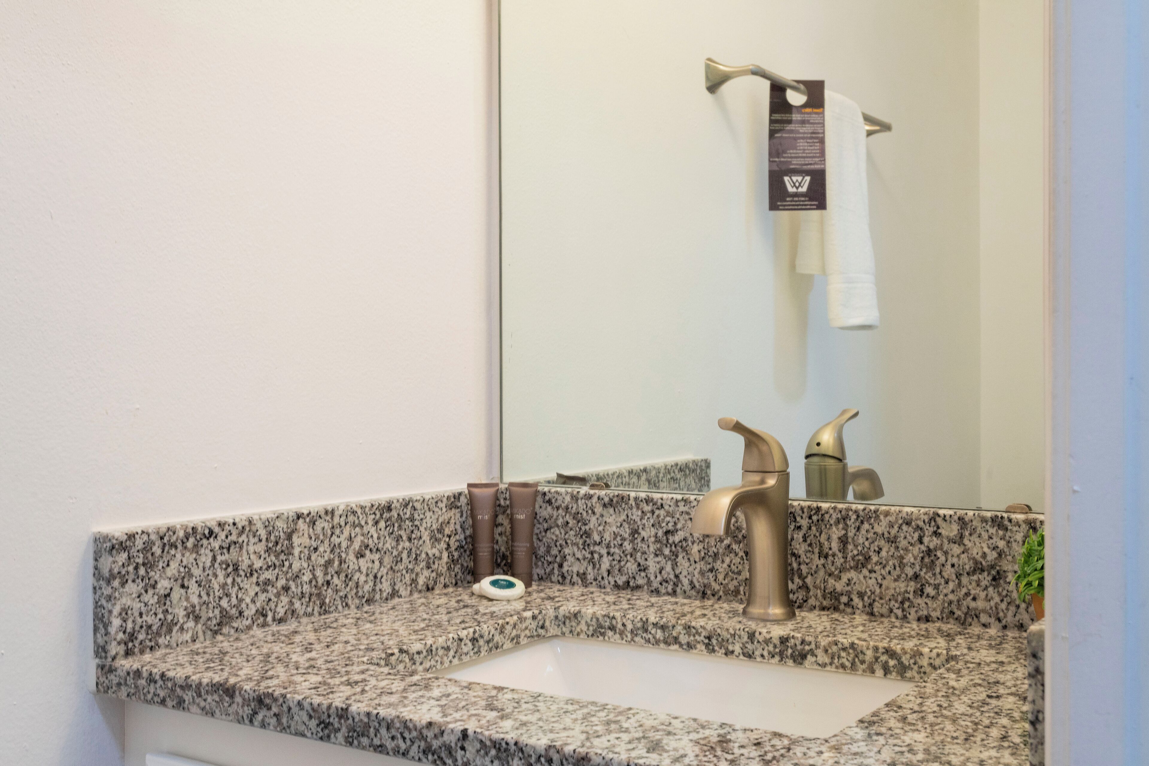 Une salle de bain avec un comptoir en granit, un lavabo, un miroir et un porte-serviettes.
