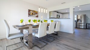 A modern kitchen with stainless steel appliances, a dining area with white chairs and a wooden table, and a painting on the wall. - Beautiful 5Bd Single Family w Game Room 106 Lake Wilson Preserve (Davenport)