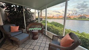 A covered balcony with wicker furniture, a patterned rug, and a view of a body of water and distant buildings. - Casa Bella at Sea Place (St. Augustine)