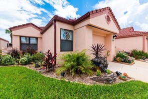 A two-story house with a red roof, a small front porch, and a well-maintained garden with various plants and a bird bath. - Casa Bella at Sea Place (St. Augustine)