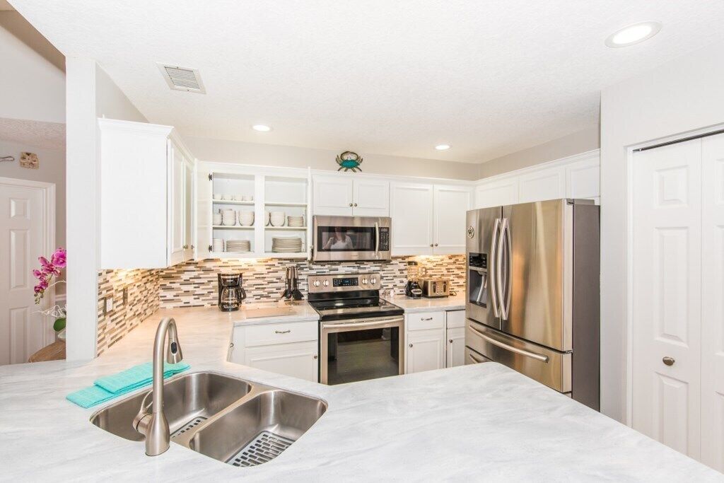 A modern kitchen with white cabinets, stainless steel appliances, and a marble countertop.