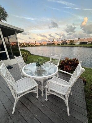 A deck with a round glass table and white wicker chairs, overlooking a body of water and a residential area. - Casa Bella at Sea Place (St. Augustine)