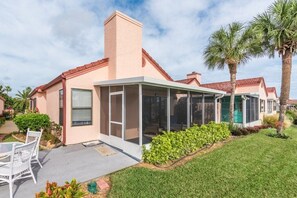 A single-story house with a covered patio, a small garden, and palm trees. - Casa Bella at Sea Place (St. Augustine)