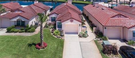 A residential area with houses featuring red-tiled roofs, a central pathway, and a body of water in the background.