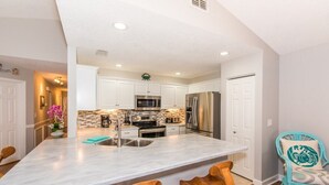 A modern kitchen with white cabinets, stainless steel appliances, and a marble island with bar stools. - Casa Bella at Sea Place (St. Augustine)