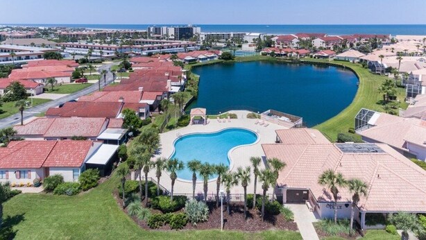 A resort with a large swimming pool surrounded by villas with red roofs, a clear view of the ocean, and a well-maintained lawn area. - Casa Bella at Sea Place (St. Augustine)