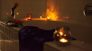 A dimly lit room with a bathtub, candles, and a flower arrangement. - Mister C Guest House (Hartbeespoort)