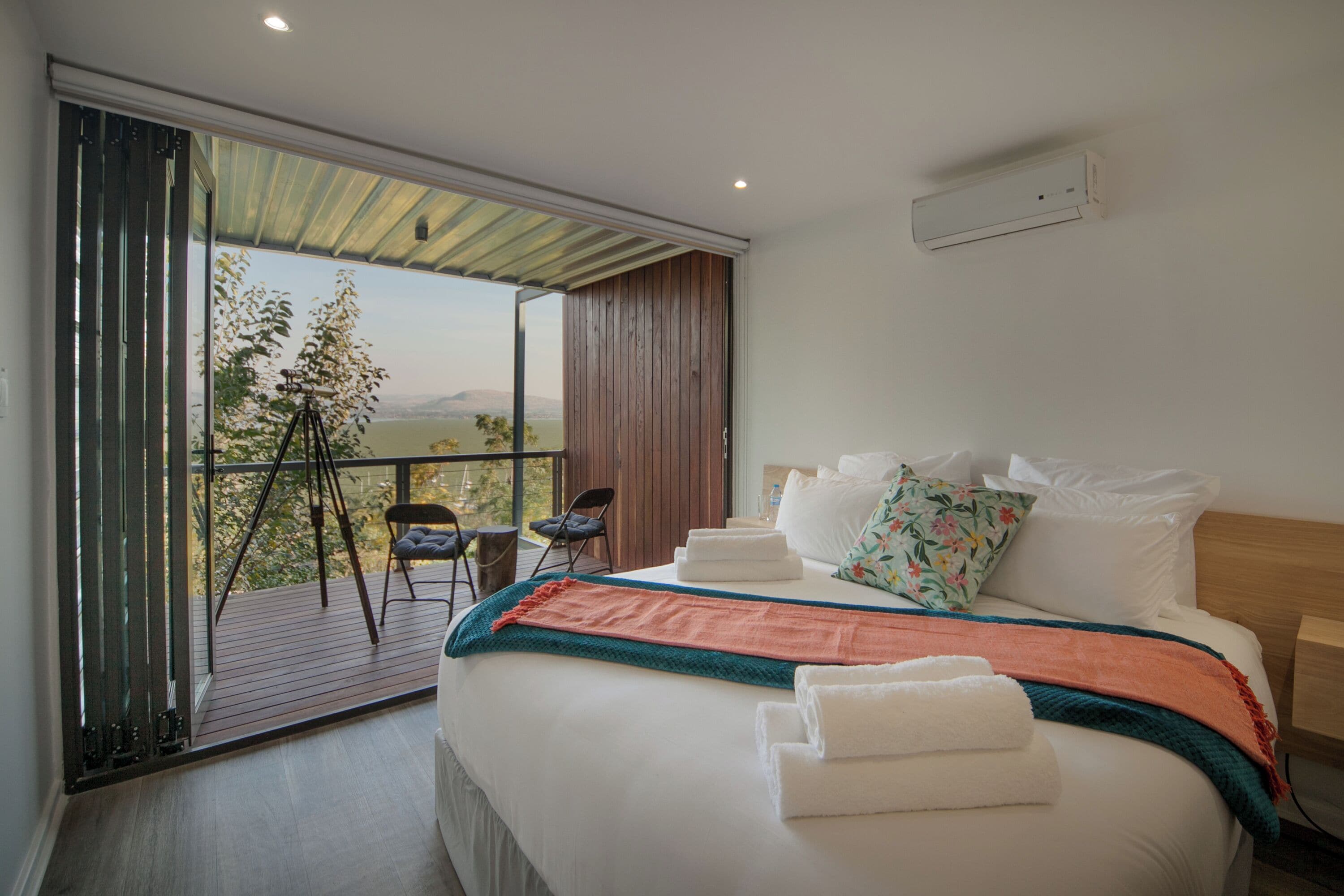 A bedroom with a large bed, a balcony with a chair, and a view of the outdoors.