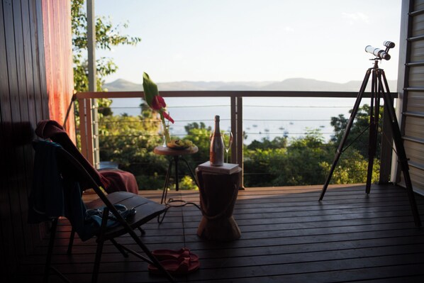 A wooden deck with a chair, a table with a bottle and glass, and a telescope.