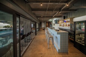Una zona de bar con taburetes, una barra y un refrigerador lleno de botellas.
