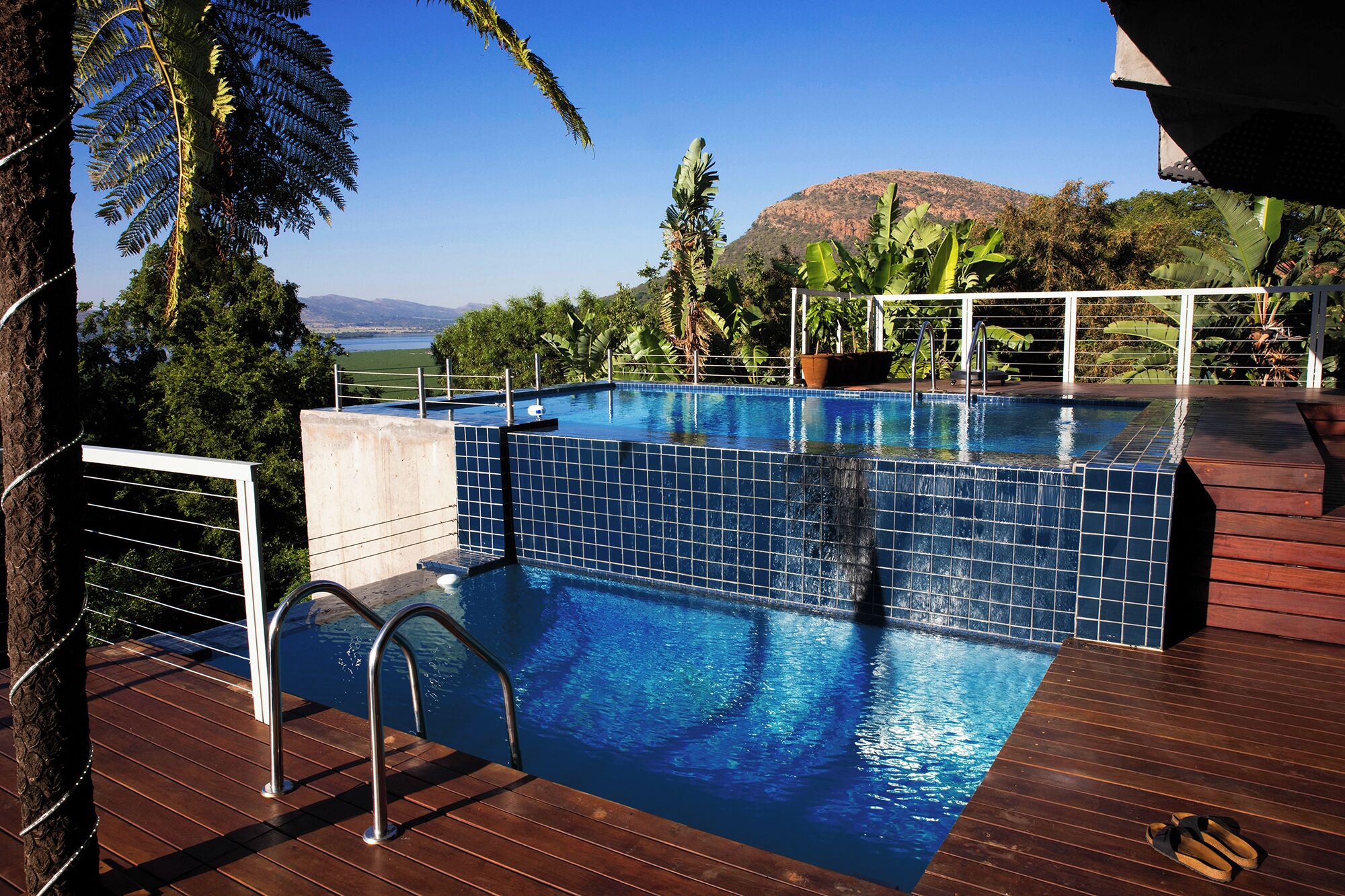 Piscina con vistas a una montaña y un lago, rodeada de plantas tropicales.