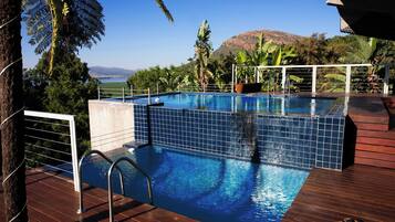 Piscina con vistas a una montaña y un lago, rodeada de plantas tropicales.