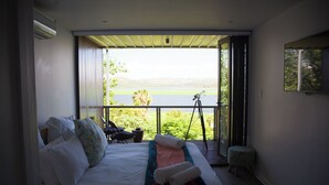 A bedroom with a large window, a telescope, and a view of a lake. - Mister C Guest House (Hartbeespoort)