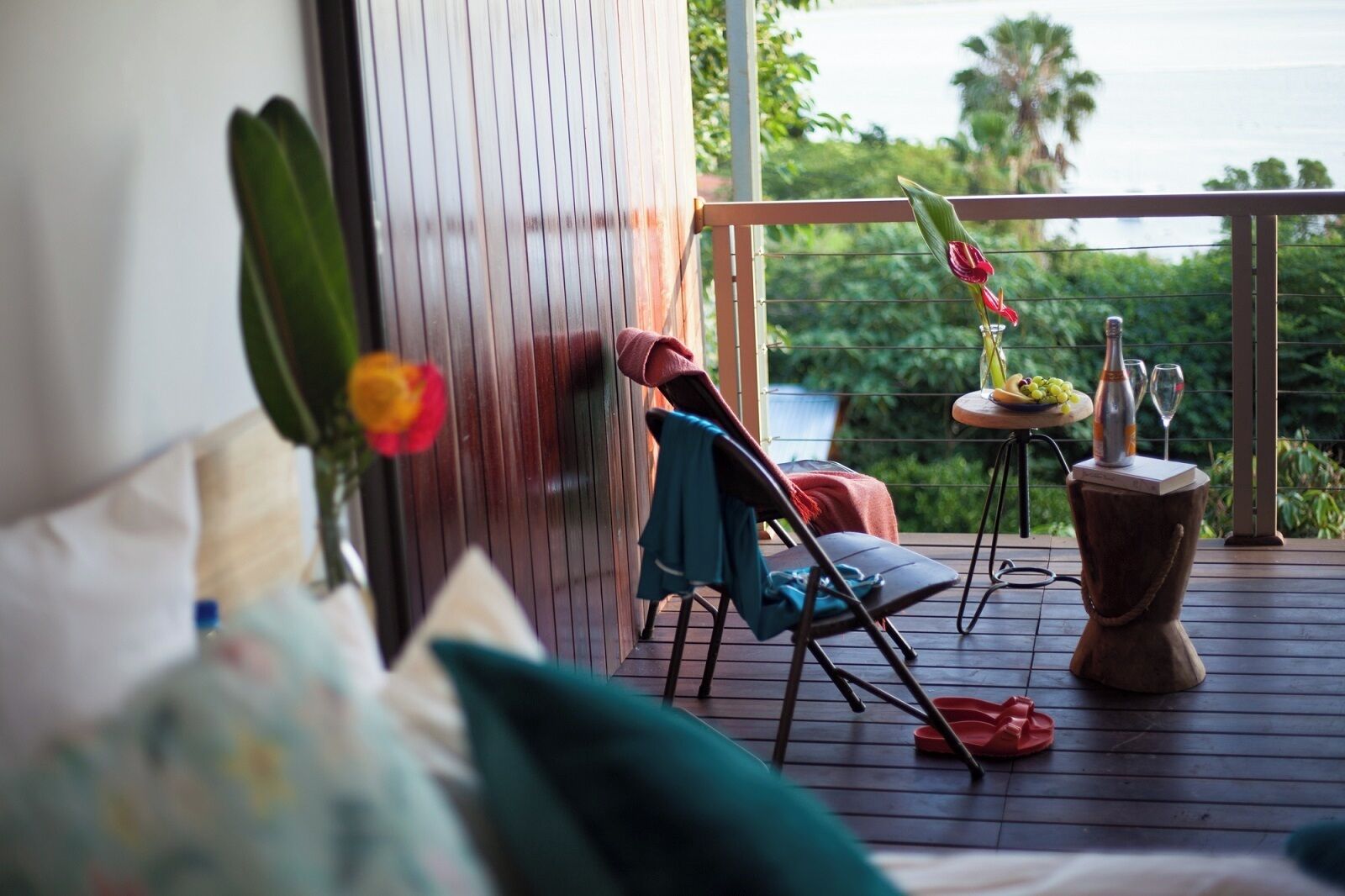 Une terrasse en bois avec une chaise, une petite table sur laquelle se trouvent une bouteille et des verres, et une plante.