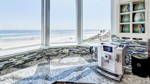 A modern bathroom with a large window overlooking a beach, a coffee machine, and a tiled backsplash. - Ocean Paradise (St. Augustine)