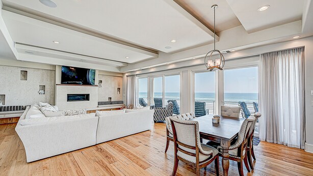 A spacious living area with a large white sofa, a dining table with chairs, and a TV mounted on the wall. - Ocean Paradise (St. Augustine)