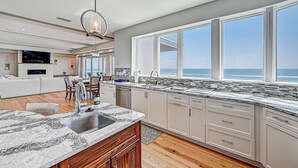 A modern kitchen with a large island, wooden cabinets, and a view of the ocean. - Ocean Paradise (St. Augustine)