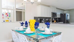 A modern kitchen with white cabinets, a black refrigerator, and a glass dining table with white chairs. - Family Friendly 2 Bd Close to Disney Storey Lake 105 3161 (Kissimmee)