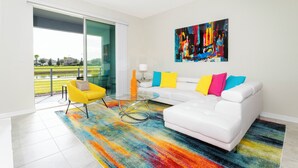 A modern living room with a white sofa, colorful cushions, a glass coffee table, and a vibrant rug. - Family Friendly 2 Bd Close to Disney Storey Lake 105 3161 (Kissimmee)