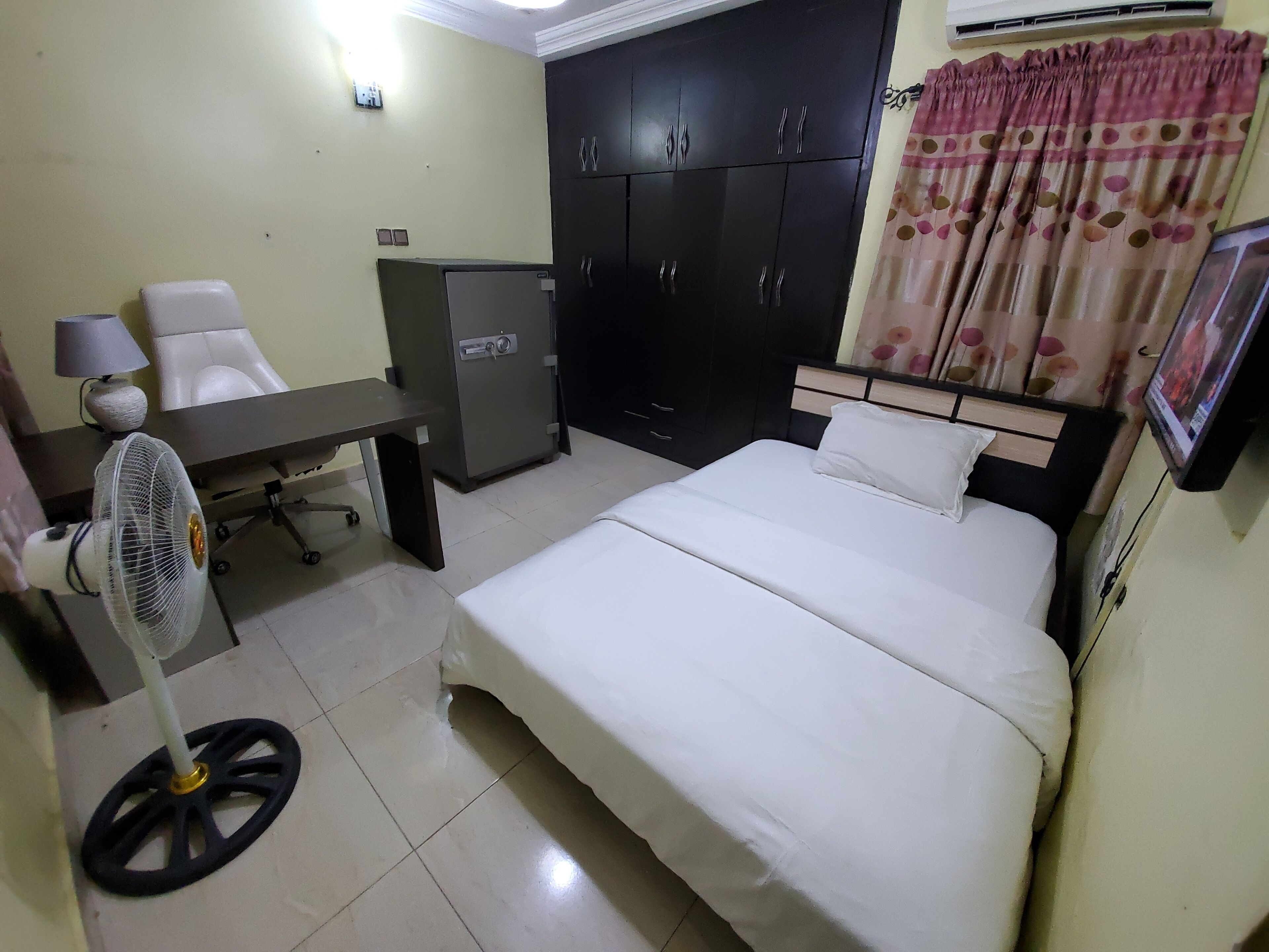 A hotel room with a bed, desk, chair, and a safe.