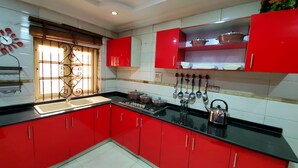 Une cuisine avec des meubles de rangement rouges, une cuisinière à gaz et une fenêtre ornée de barreaux en fer décoratifs.