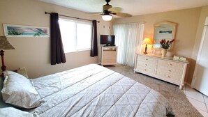 Un dormitorio con cama, cómoda, televisor y ventilador de techo.
