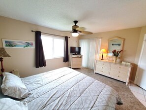 Comfortable bedroom with a large bed, ceiling fan, dresser, and TV.