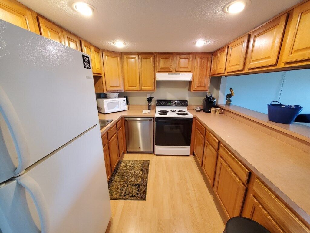 A compact kitchen with wooden cabinets, a refrigerator, a microwave, a dishwasher, and a stove.