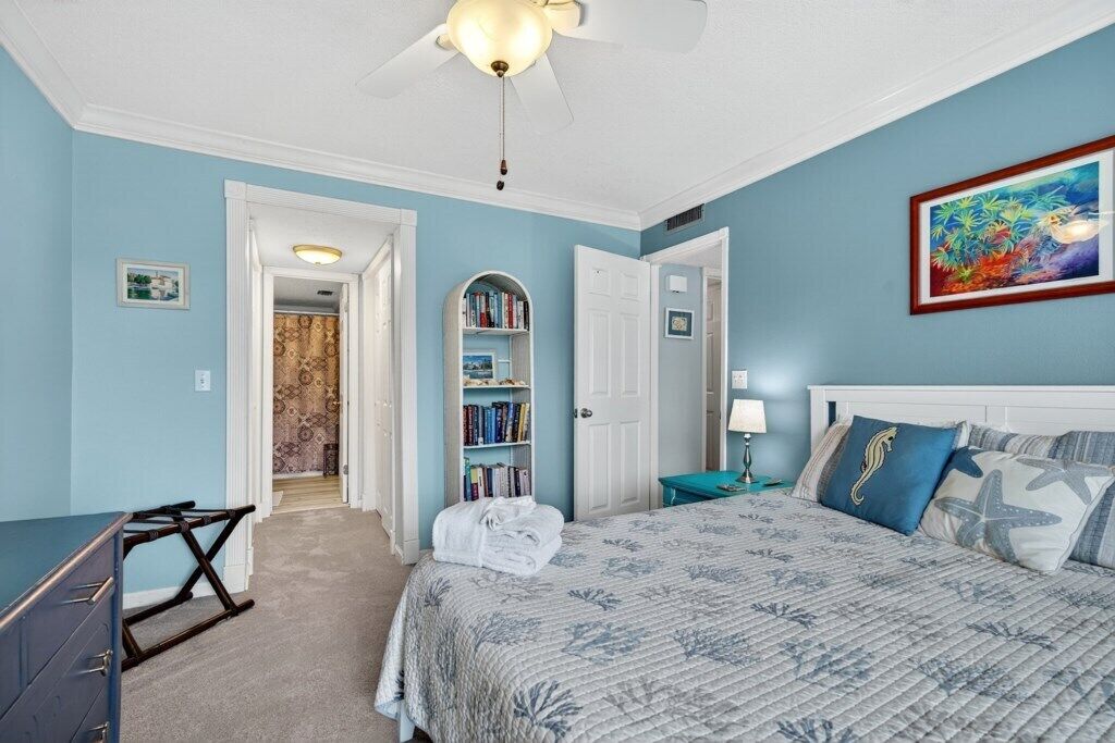 A bedroom with a bed, a desk, a bookshelf, and a ceiling fan.