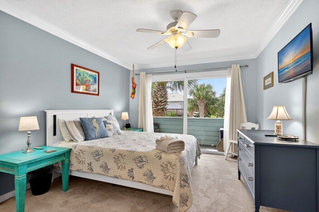 A bedroom with a bed, a desk, a chair, a ceiling fan, and a window with curtains.