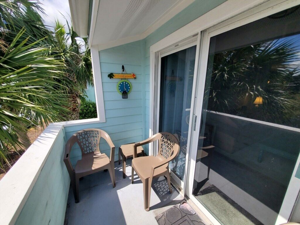 A covered outdoor area with two chairs and a small table, a sliding glass door, and a wall clock.