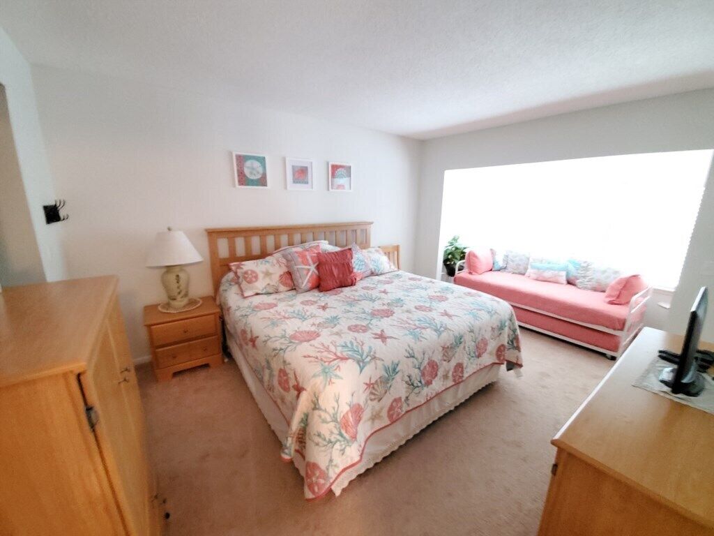 A bedroom with a bed, a nightstand, a dresser, a desk, and a window.