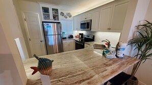 A kitchen with white cabinets, stainless steel appliances, a marble countertop, and a potted plant. - Summerhouse 104 (St. Augustine)