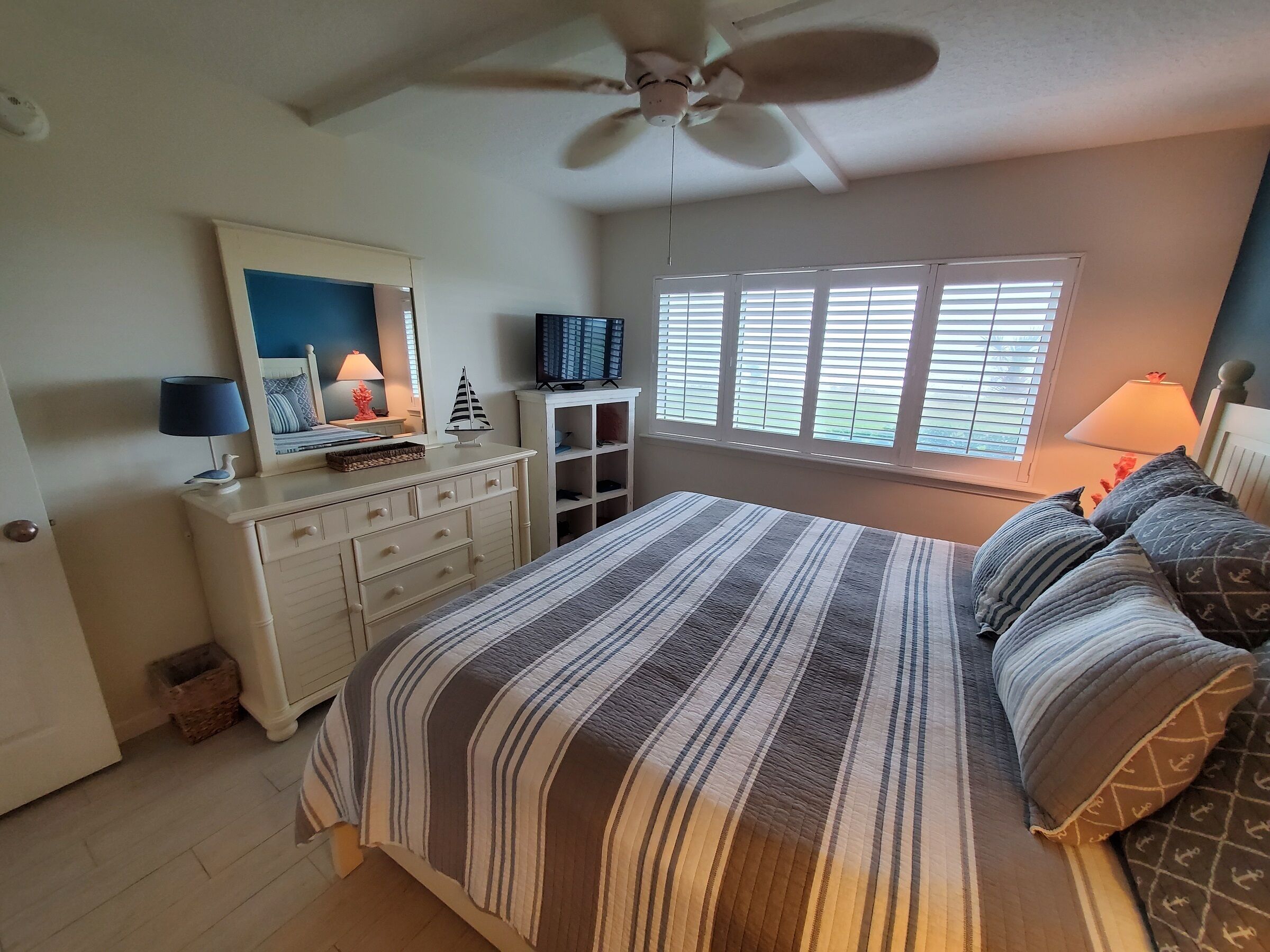 A bedroom with a bed, dresser, mirror, television, and a window with blinds.