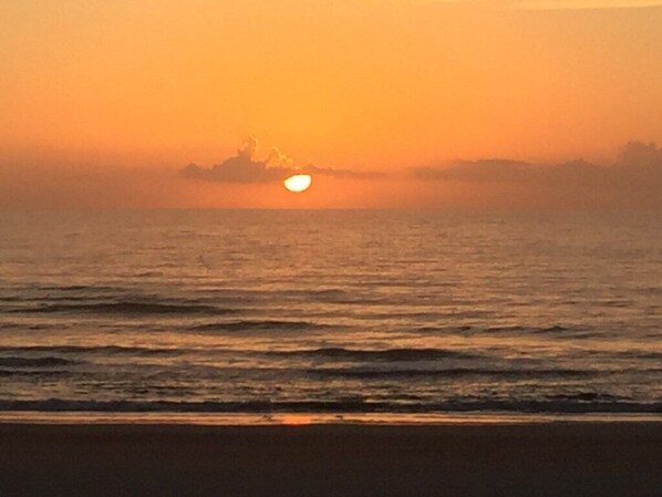 A sunset over a calm sea with a beach in the foreground.
