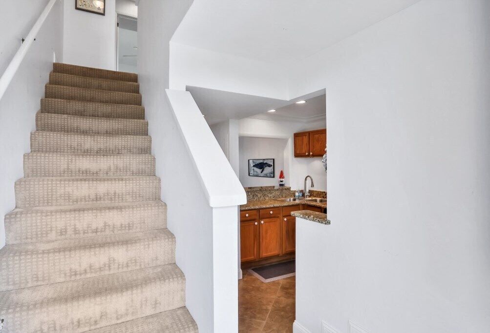 A staircase leading to a kitchen with wooden cabinets and a granite countertop.
