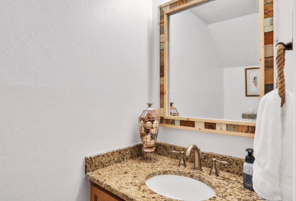 A bathroom with a granite countertop, a sink, a mirror with a wooden frame, and a towel hanging on the wall.