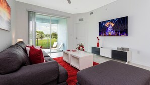 A modern living room with a grey sofa set, a white coffee table, and a red rug. There is a large window with a view of greenery outside. - Gorgeous 3Bd 8 Guests Storey Lake Resort Close to Disney 101 3191 (Kissimmee)