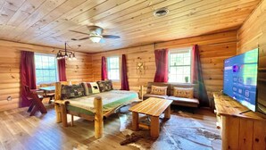 A log cabin interior with a bed, sofa, wooden coffee table, and a television. - 5 min from Parkway. Cozy cabin! (Sevierville)