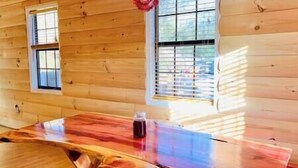 A wooden cabin interior with a large dining table, two windows, and a view of the outdoors. - 5 min from Parkway. Cozy cabin! (Sevierville)
