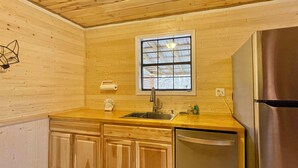 A compact kitchen with wooden cabinets, a stainless steel sink, and a built-in dishwasher. - 5 min from Parkway. Cozy cabin! (Sevierville)