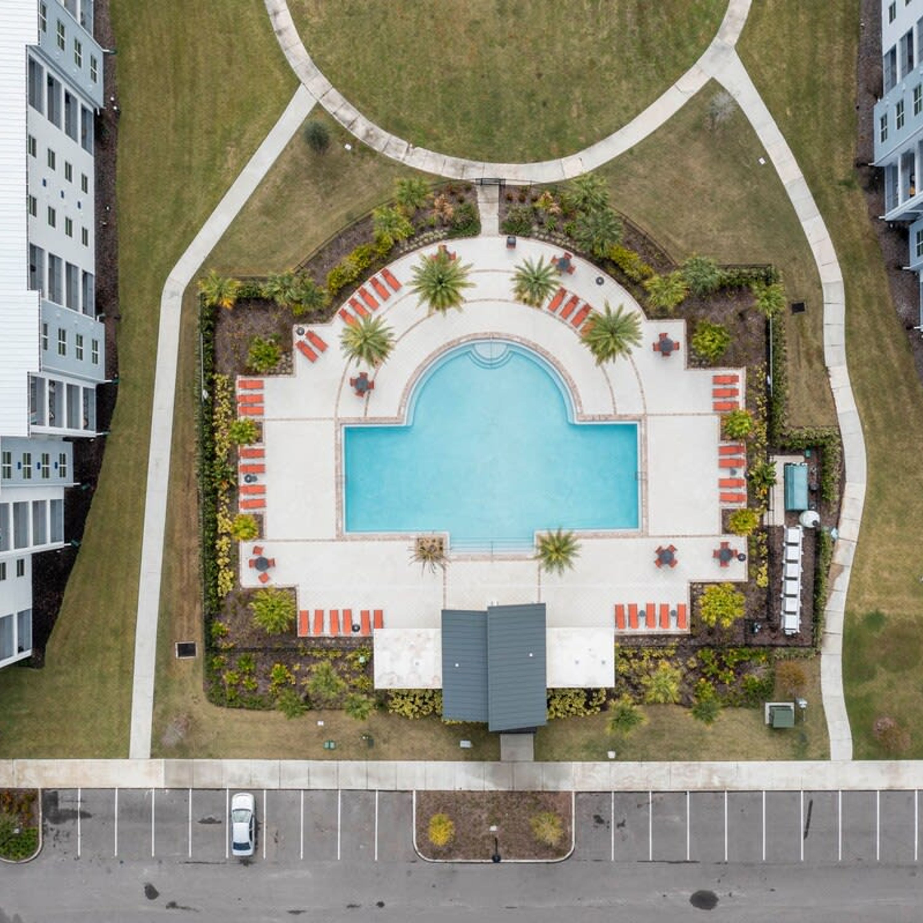 Ein Luftbild eines Wohngebiets mit einem zentral gelegenen Schwimmbad, umgeben von Liegestühlen und Palmen.
