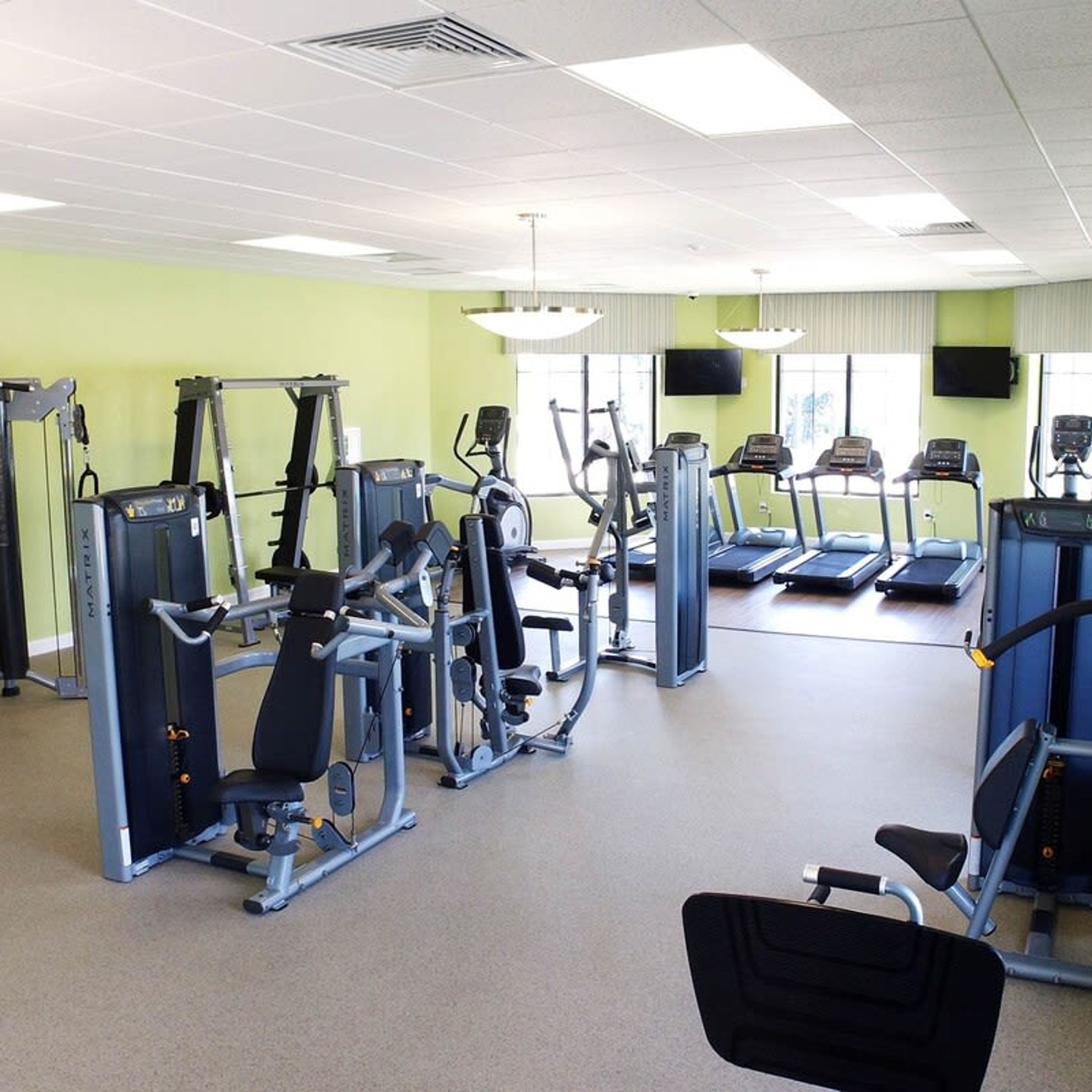A gym with various exercise machines, treadmills, and a mirrored wall.