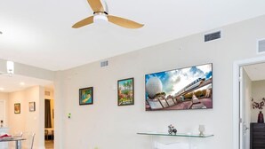 A modern living room with a ceiling fan, a dining area with a glass table, and a large TV displaying a space-themed image. - Stunning 2Bd Apto Close to Disney Storey Lake 105 3171 (Kissimmee)